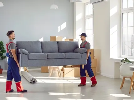 Zwei Möbelträger in Arbeitskleidung tragen ein Sofa aus einer Wohnung